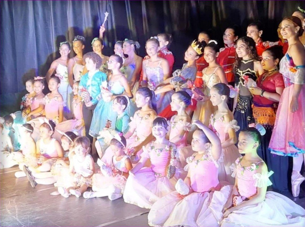 Elenco infantil e jovens bailarinas reunidos no palco após uma apresentação.